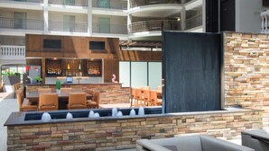 An outdoor bar area with stone walls, wooden furniture, and a view of the building's interior balconies. - Embassy Suites by Hilton Colorado Springs (Colorado Springs)
