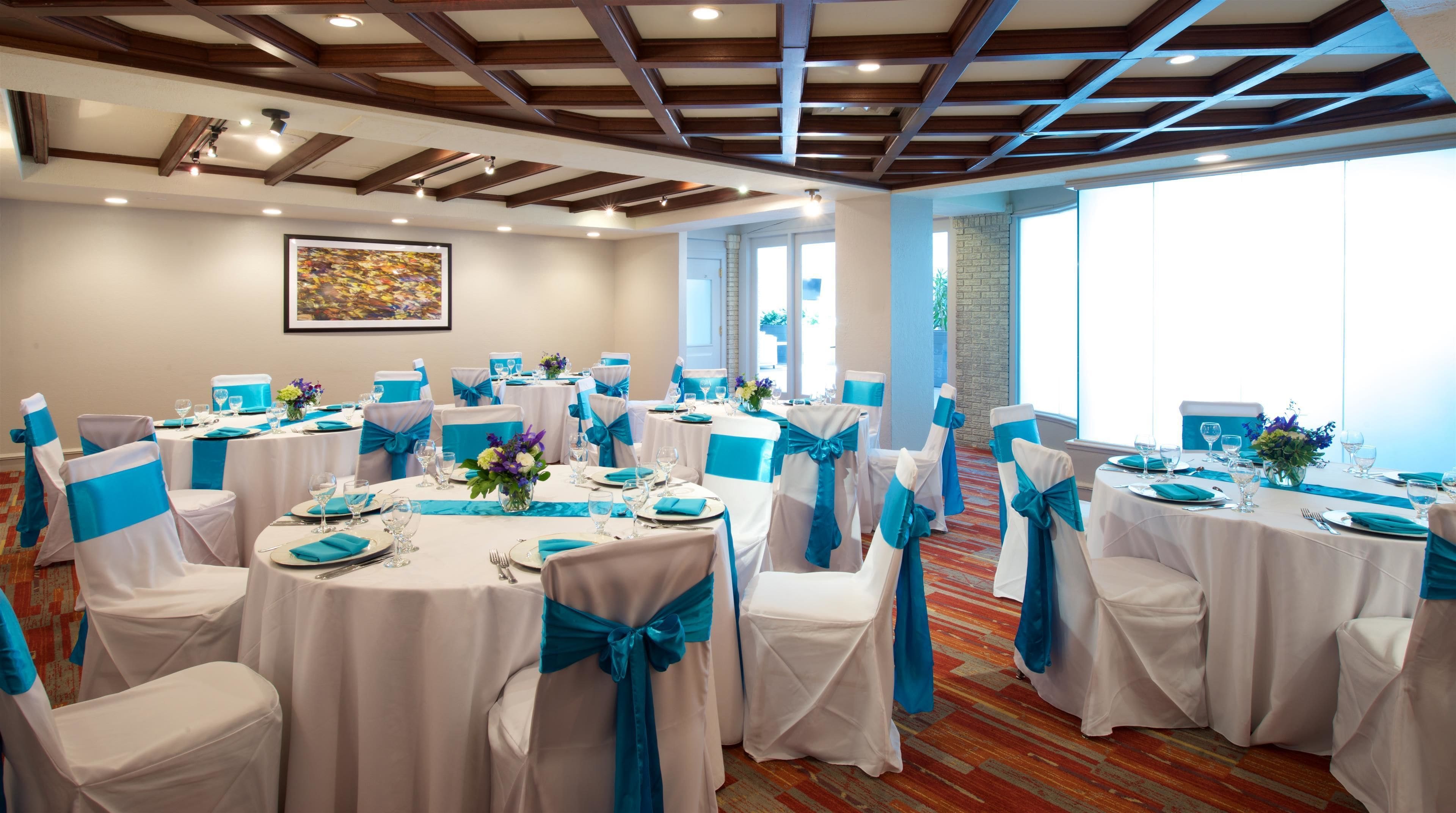 A conference room with round tables, chairs with blue sashes, and a large window providing natural light.
