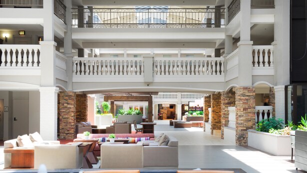 A spacious indoor lobby with multiple seating areas, a central fountain, and a view of the lower level. - Embassy Suites by Hilton Colorado Springs (Colorado Springs)