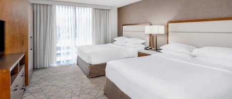 Ein Hotelzimmer mit zwei Betten, einem Holzschrank, einem Schreibtisch und einem großen Fenster mit Vorhängen.