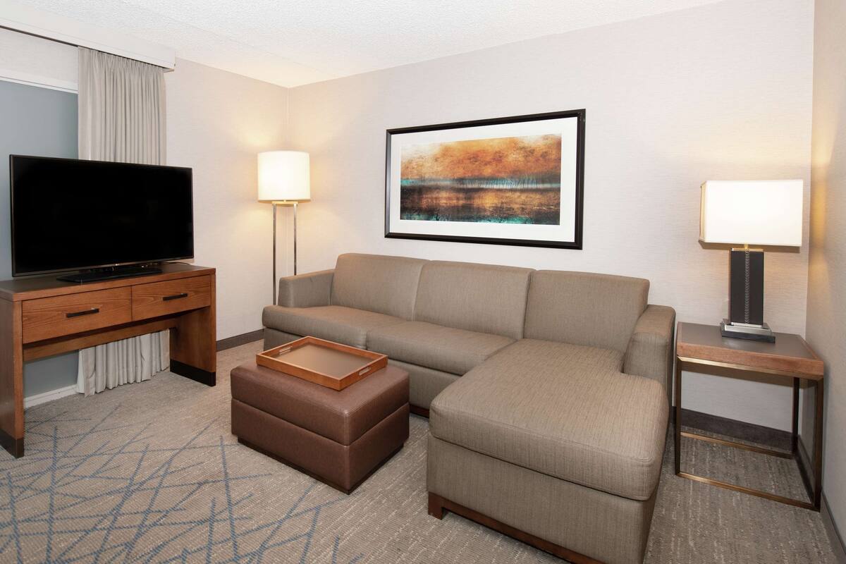 A hotel room with a flat-screen TV, a sofa, a coffee table, and a painting on the wall.