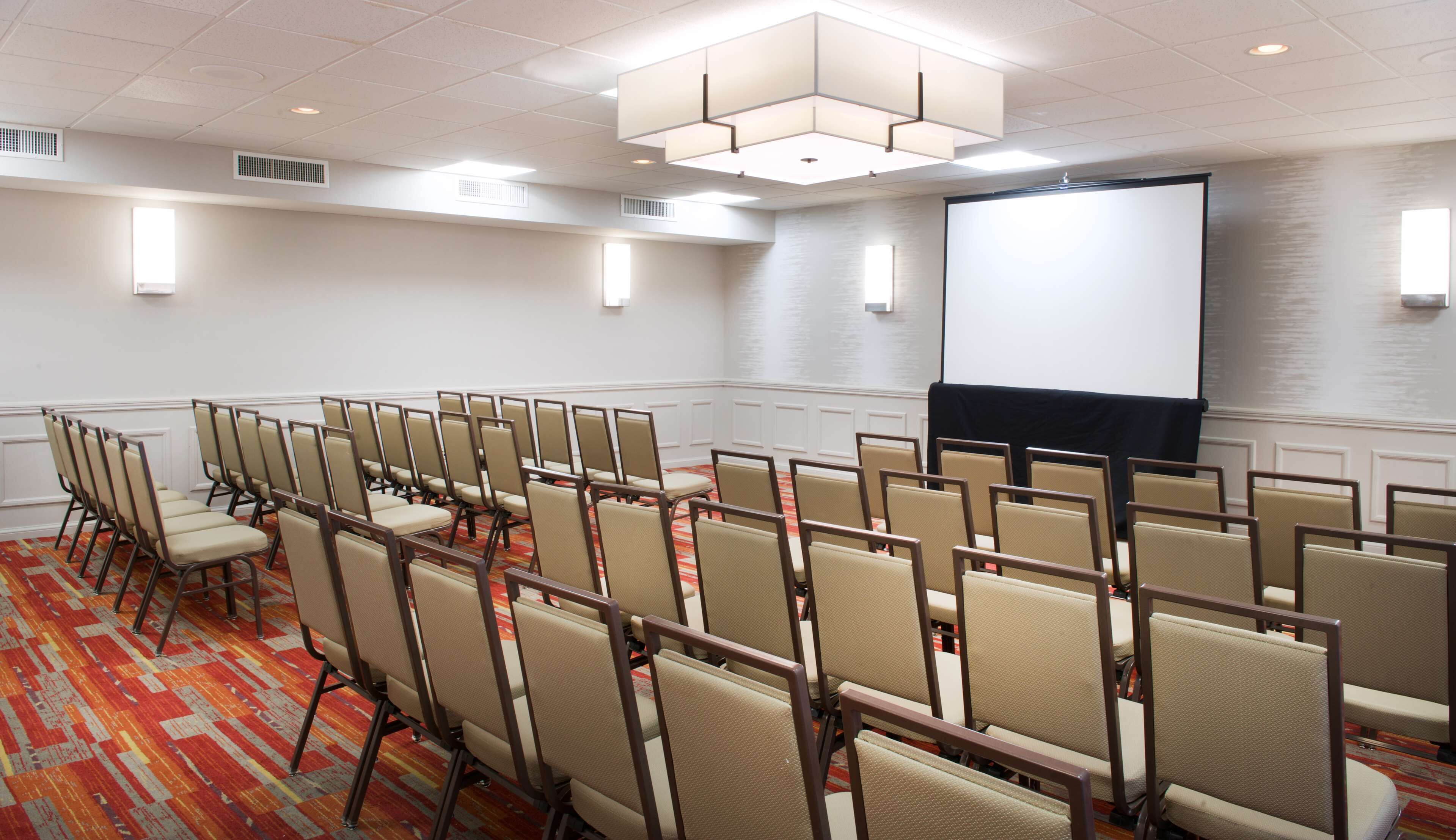 A conference room with rows of chairs, a projector screen, and a carpeted floor.