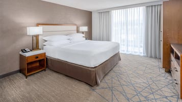 A hotel room with a large bed, two bedside tables with lamps, a wooden nightstand, a wardrobe, and a large window with curtains.