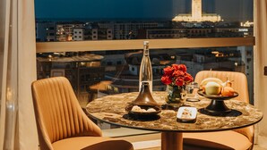 Un comedor con una mesa dispuesta para dos, un jarrón de rosas rojas y vistas a un paisaje urbano con una torre destacada.