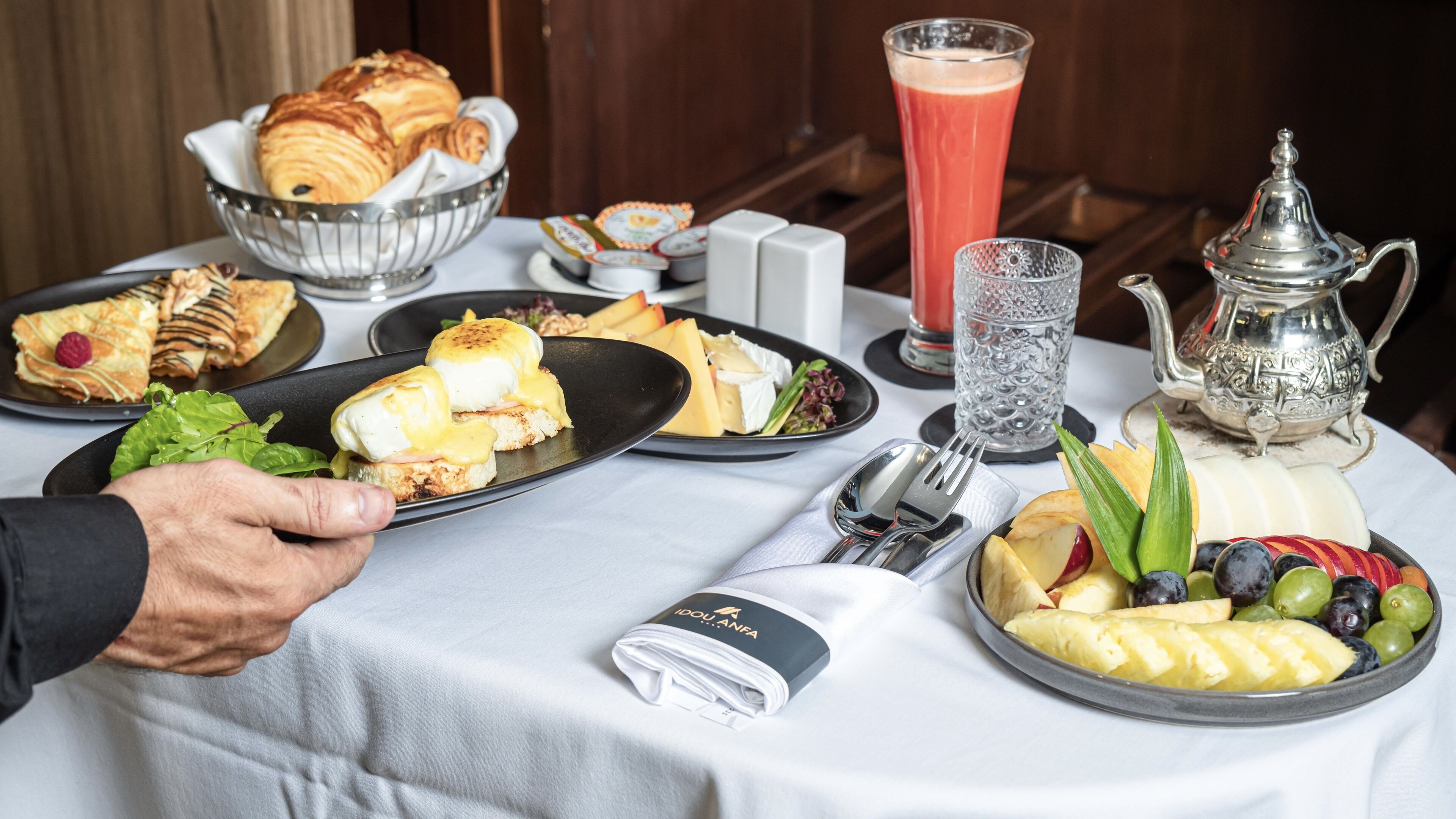 A breakfast buffet with various dishes, including pastries, cheese, fruits, and a pitcher of juice.