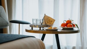 Una mesa de desayuno ordenada con una bandeja de naranjas y un cuenco decorativo, frente a una ventana con cortinas translúcidas.