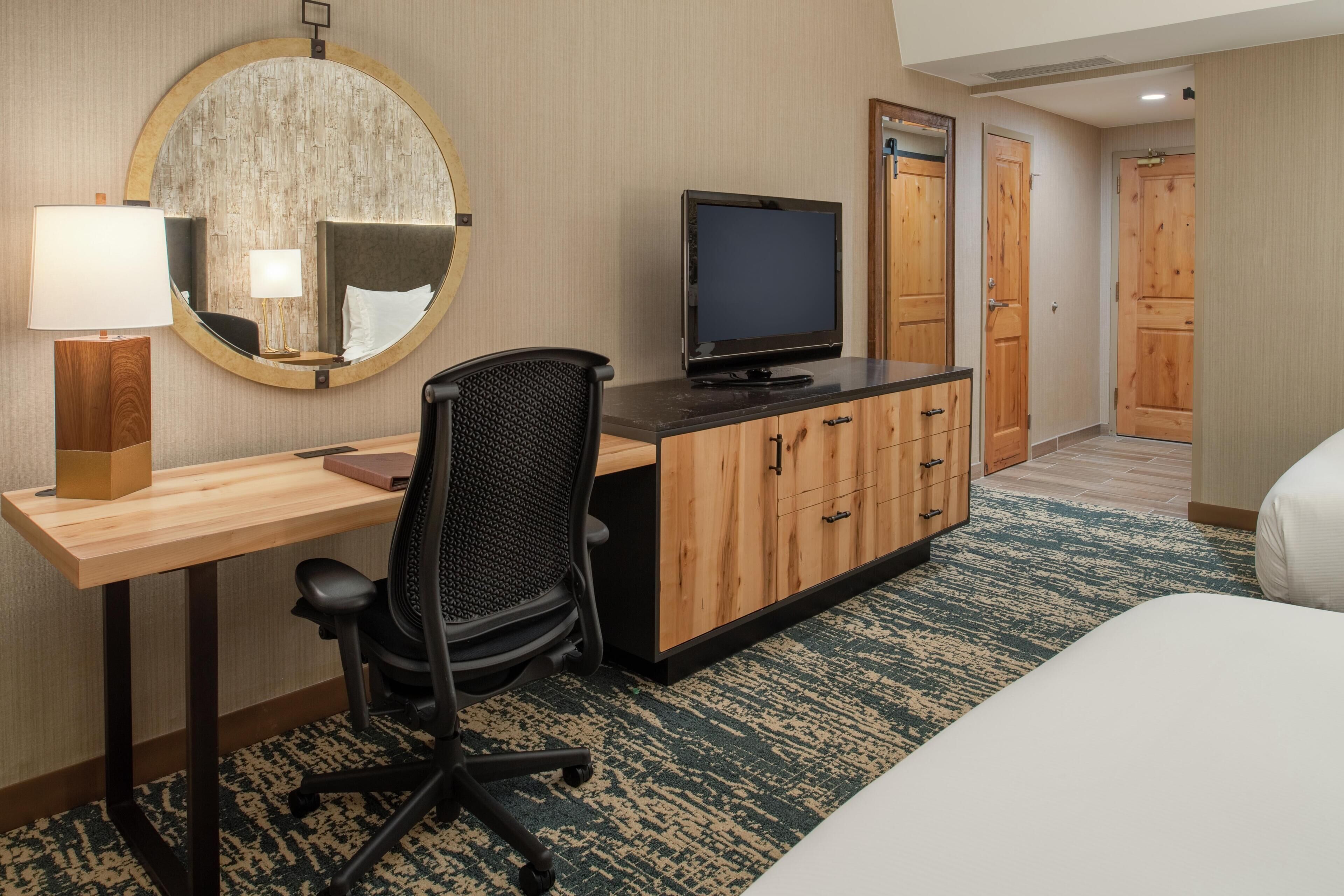A hotel room with a desk, chair, television, and a bed.