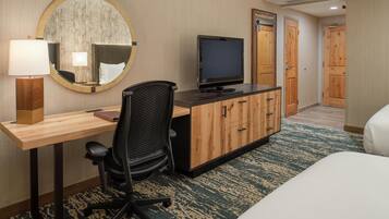 A hotel room with a desk, chair, television, and a bed.