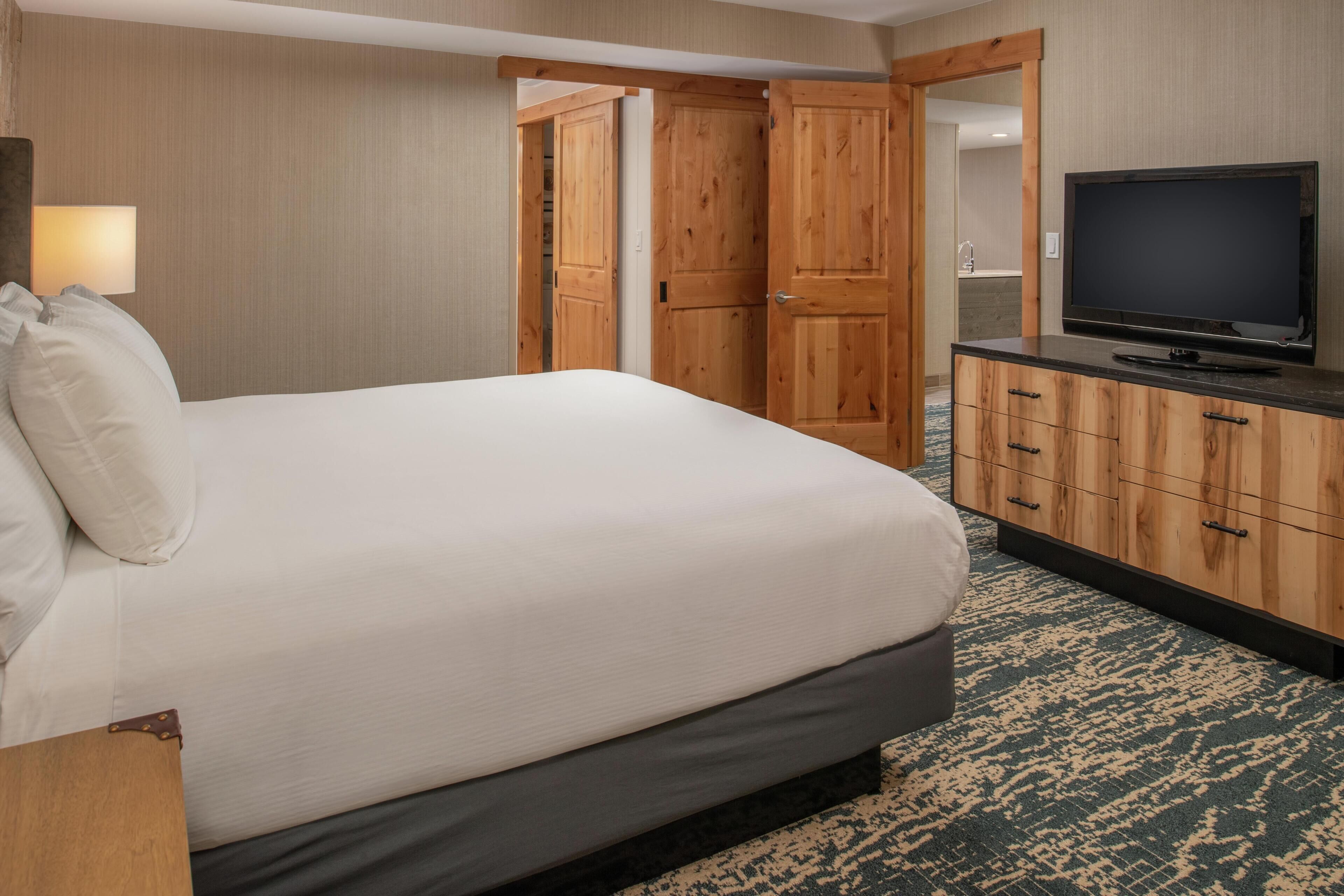 A hotel room with a bed, a television, a wooden wardrobe, and a bathroom visible through an open door.