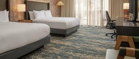 A hotel room with two beds, a desk with a chair, a TV, and a large window with curtains.