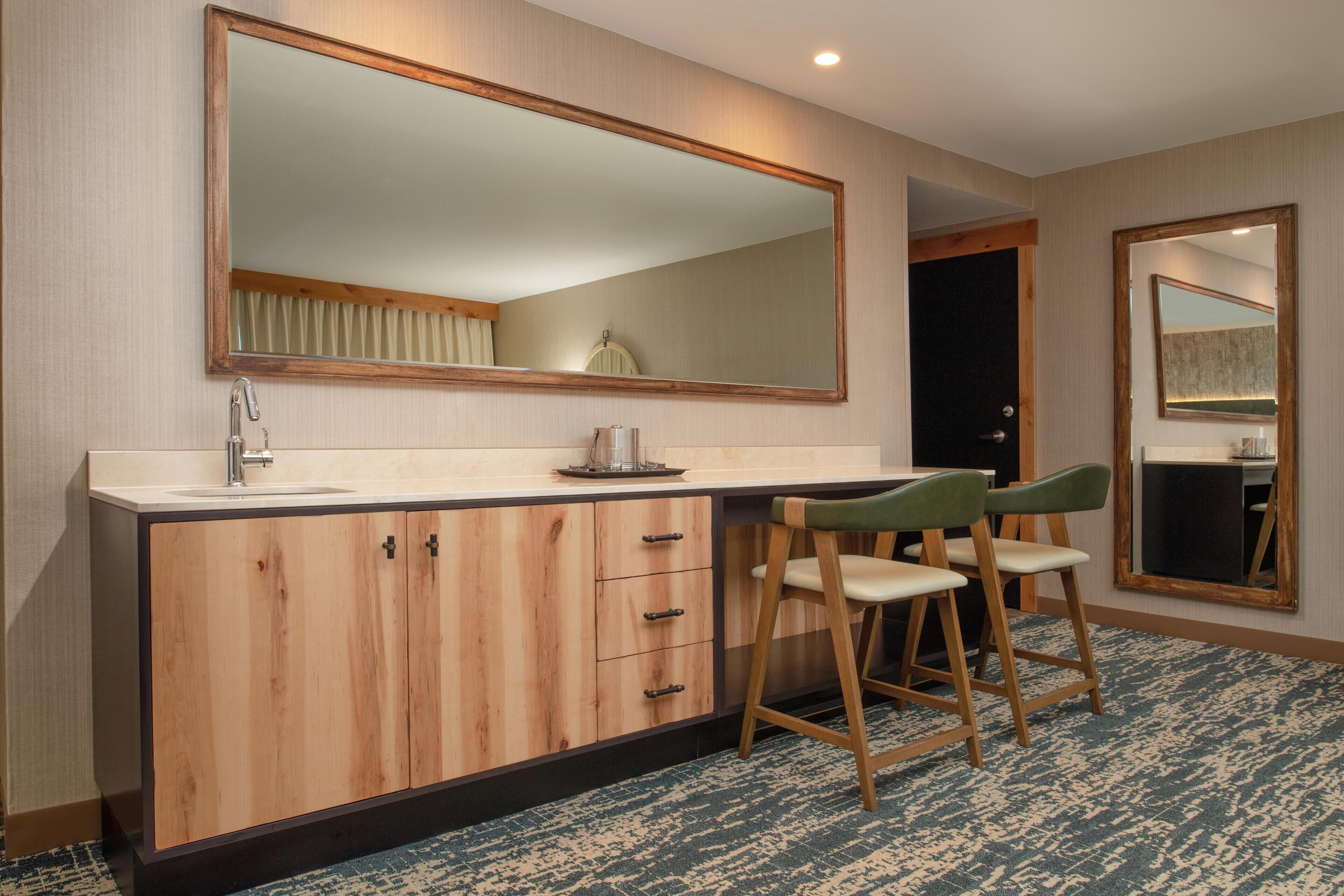 A modern bathroom with a wooden vanity, a large mirror, and two bar stools.
