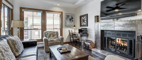 Un salon chaleureux avec une cheminée, des canapés en cuir, une table basse et un ventilateur de plafond.