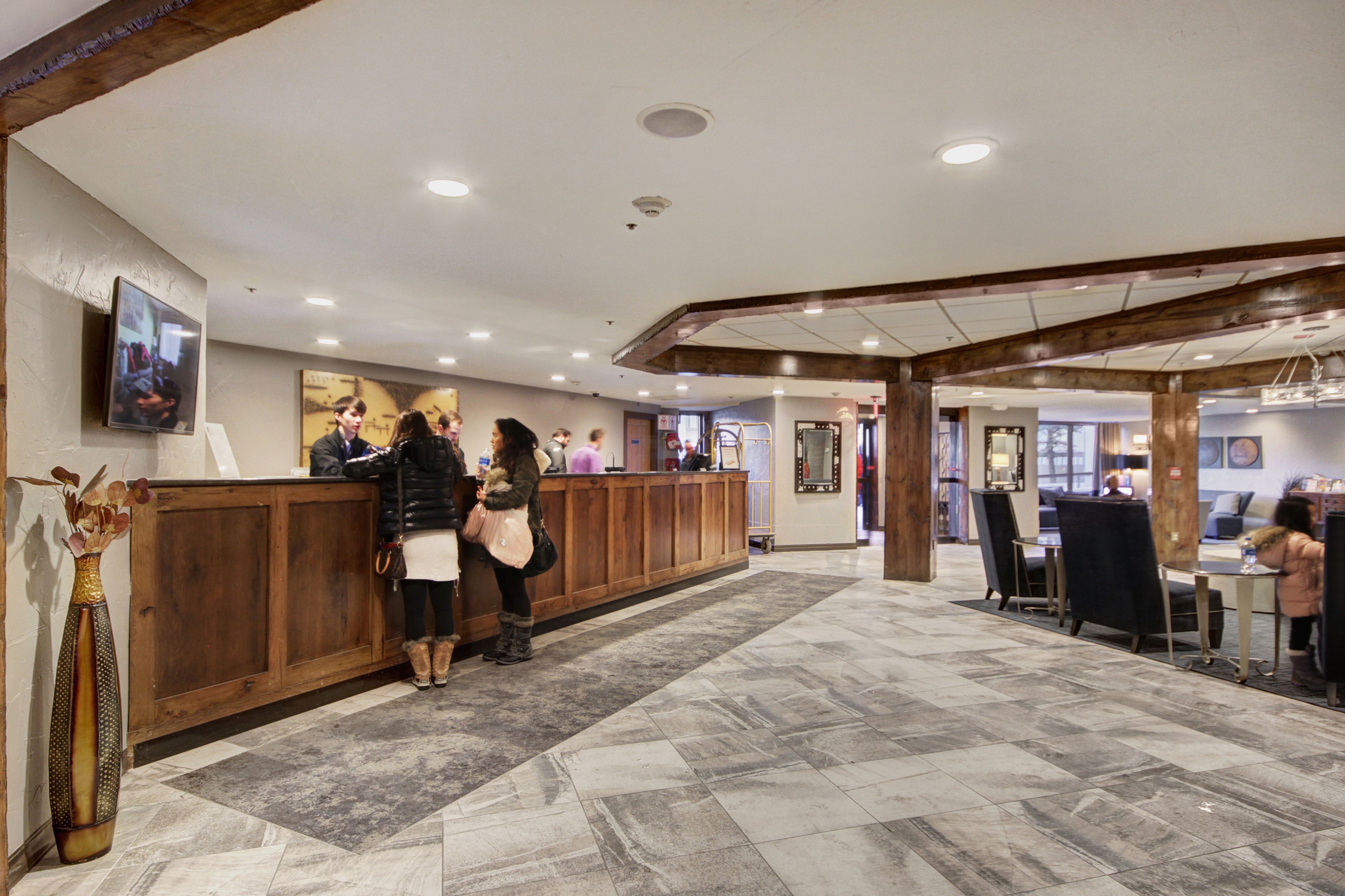 A reception area with a wooden counter, a vase with dried flowers, and a tiled floor.