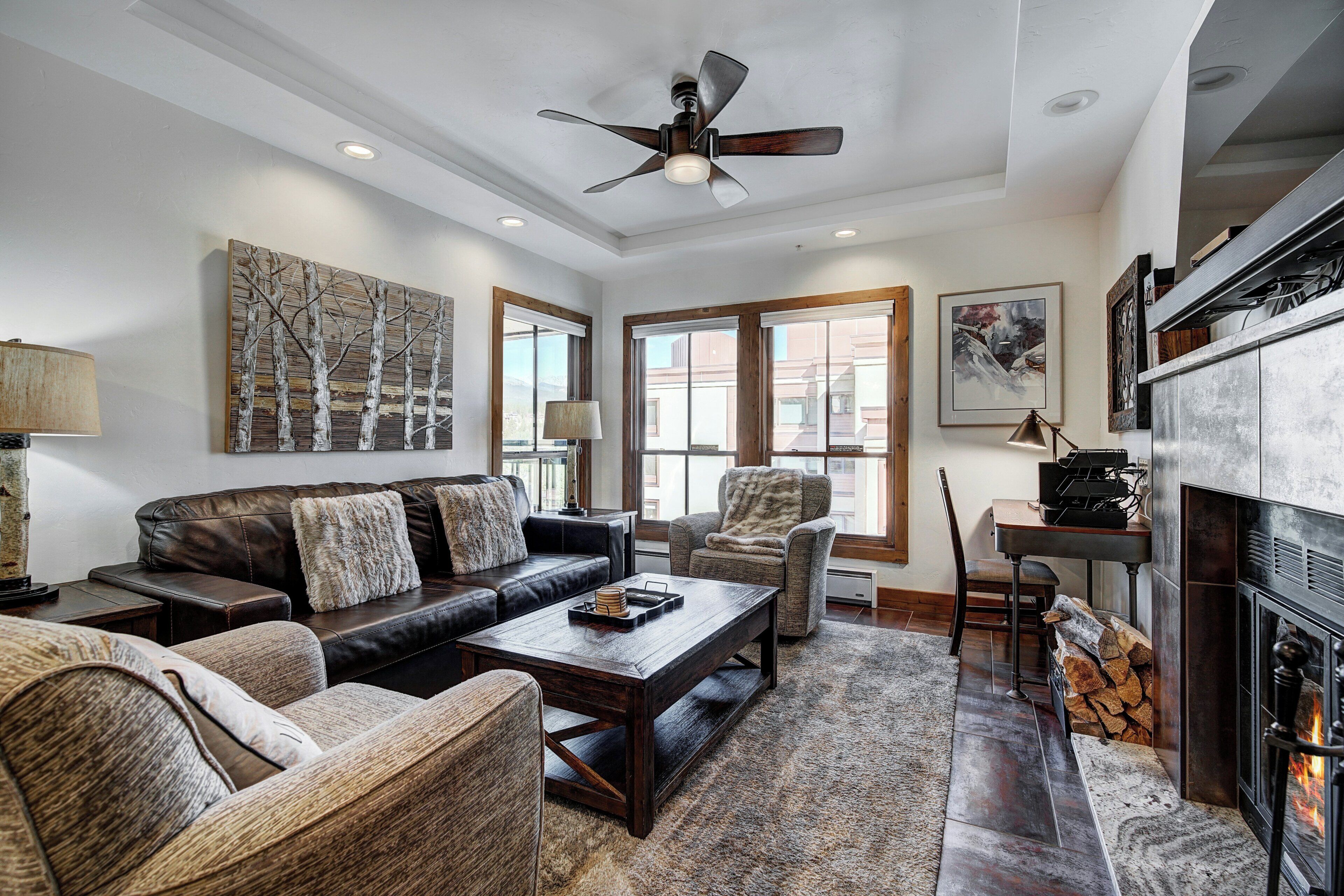 A spacious living room with a fireplace, leather sofas, a coffee table, and a large window.