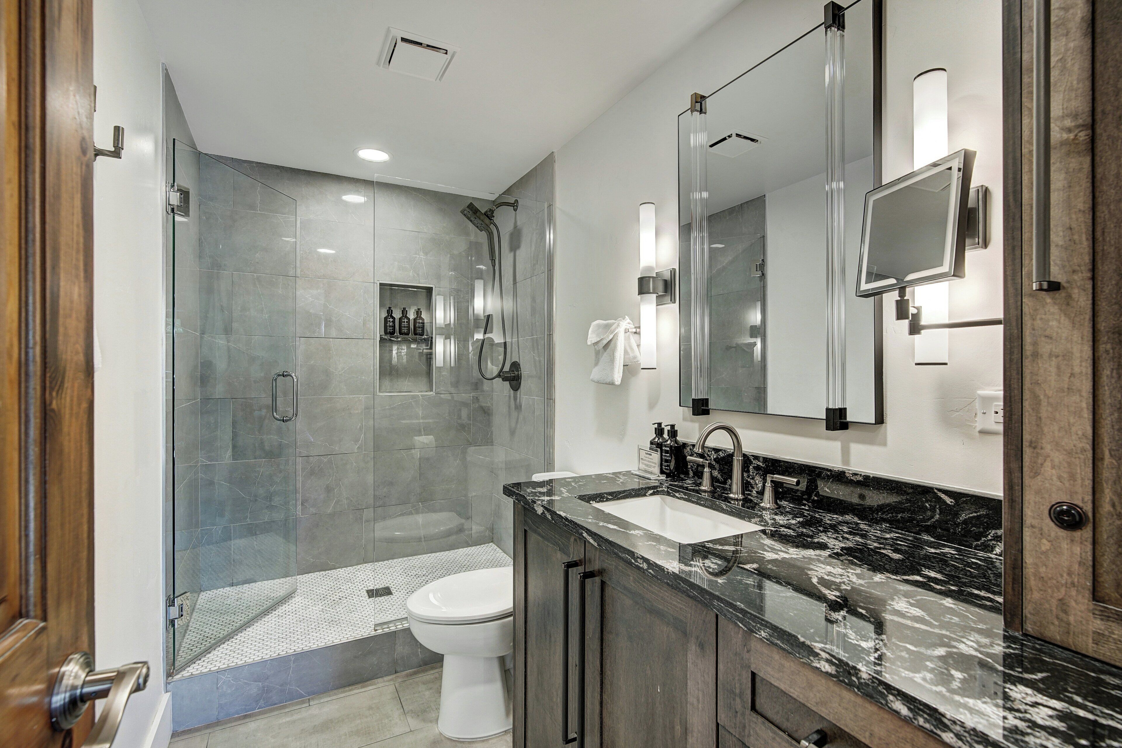 A modern bathroom with a glass-enclosed shower, a white toilet, and a marble sink.