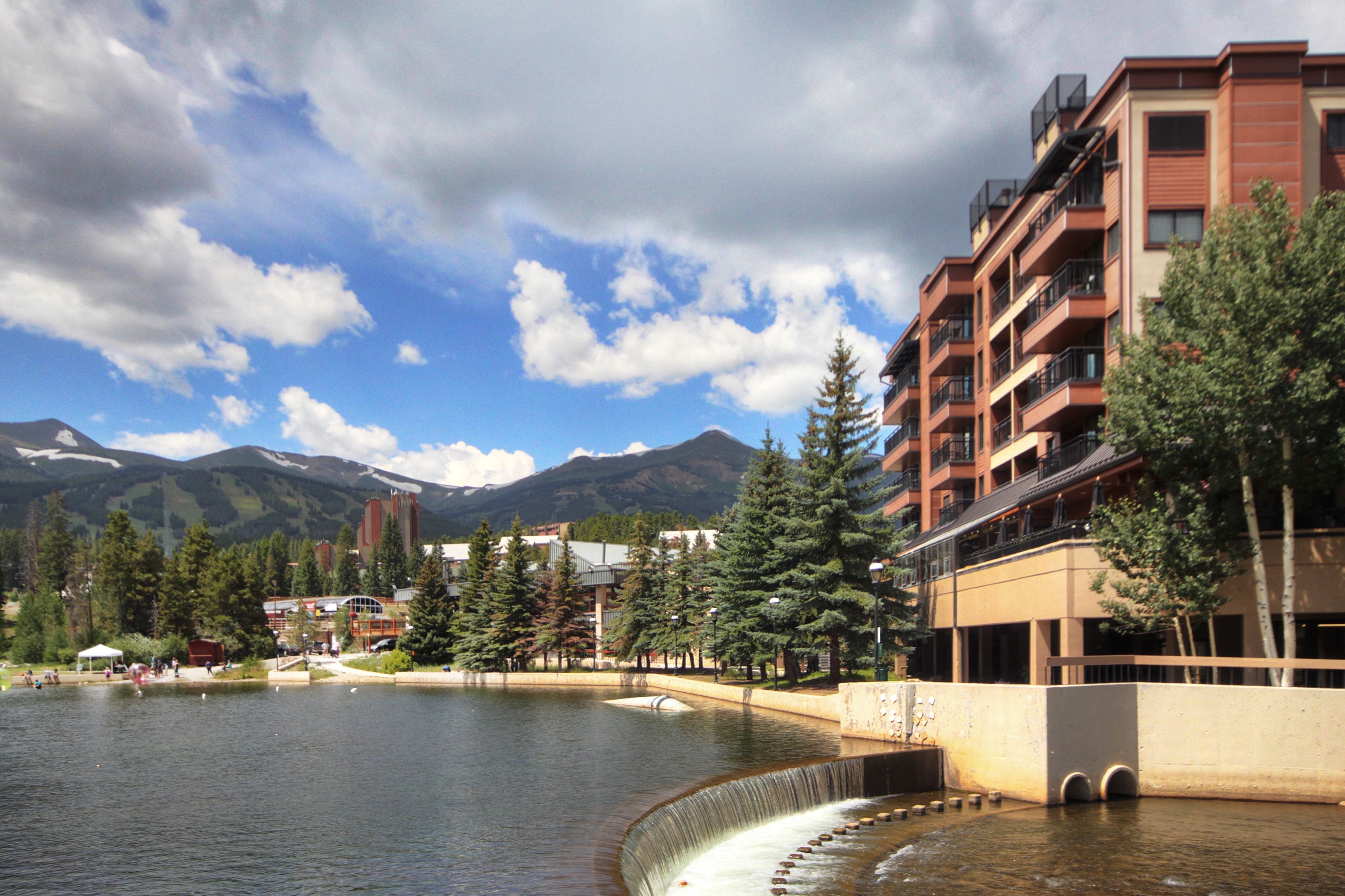 A hotel with a water feature, a mountain backdrop, and a clear sky.