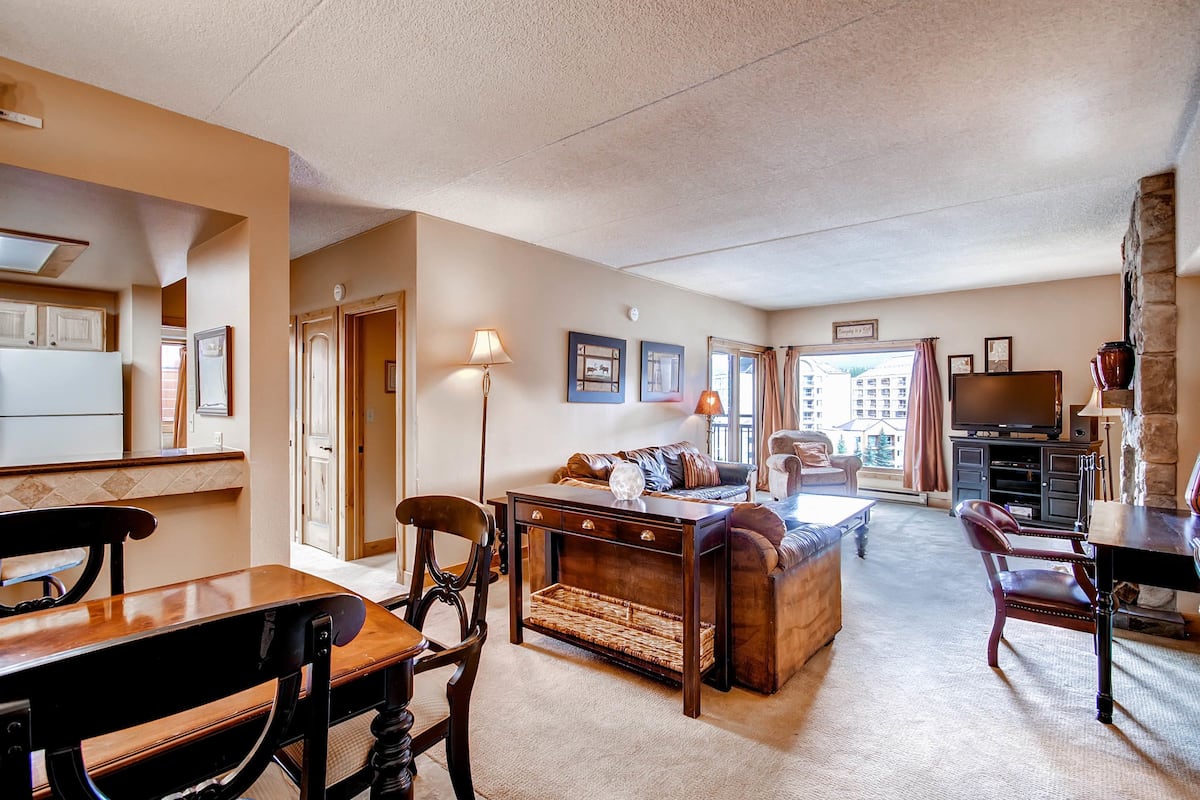 A spacious living area with a sofa, coffee table, and chairs, a kitchen with cabinets, and a television.