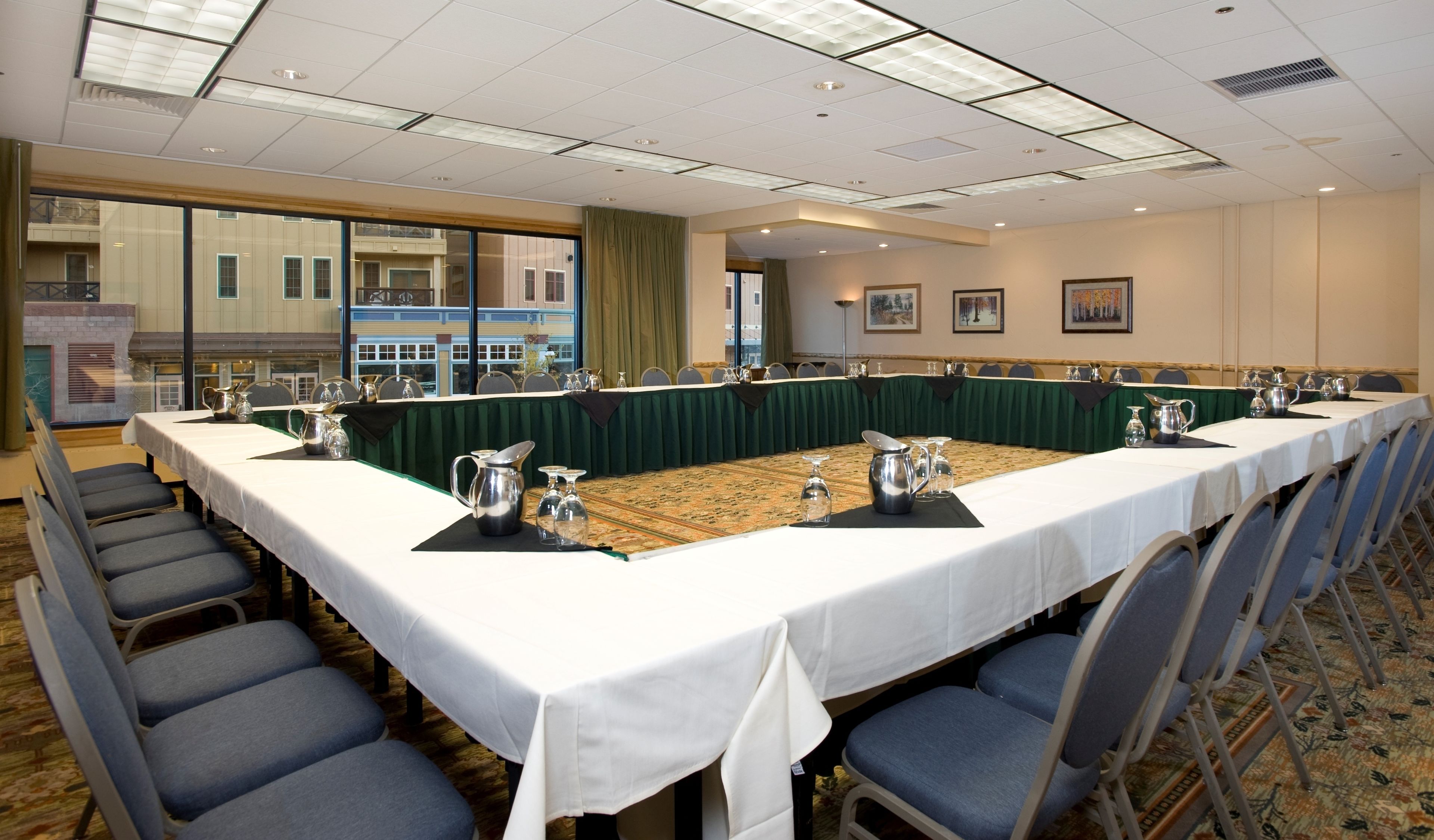 A conference room with a long table, chairs, and a view of a building through large windows.