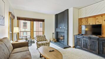 Una sala de estar con chimenea, un sofá, una mesa de centro y un televisor sobre un mueble de madera.