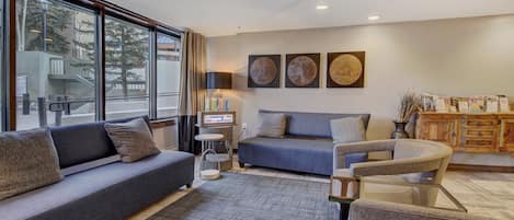 A modern living room with a sofa, armchairs, a coffee table, and a small side table. There are three wall-mounted artworks and a sign that reads "Caffeine Bar".