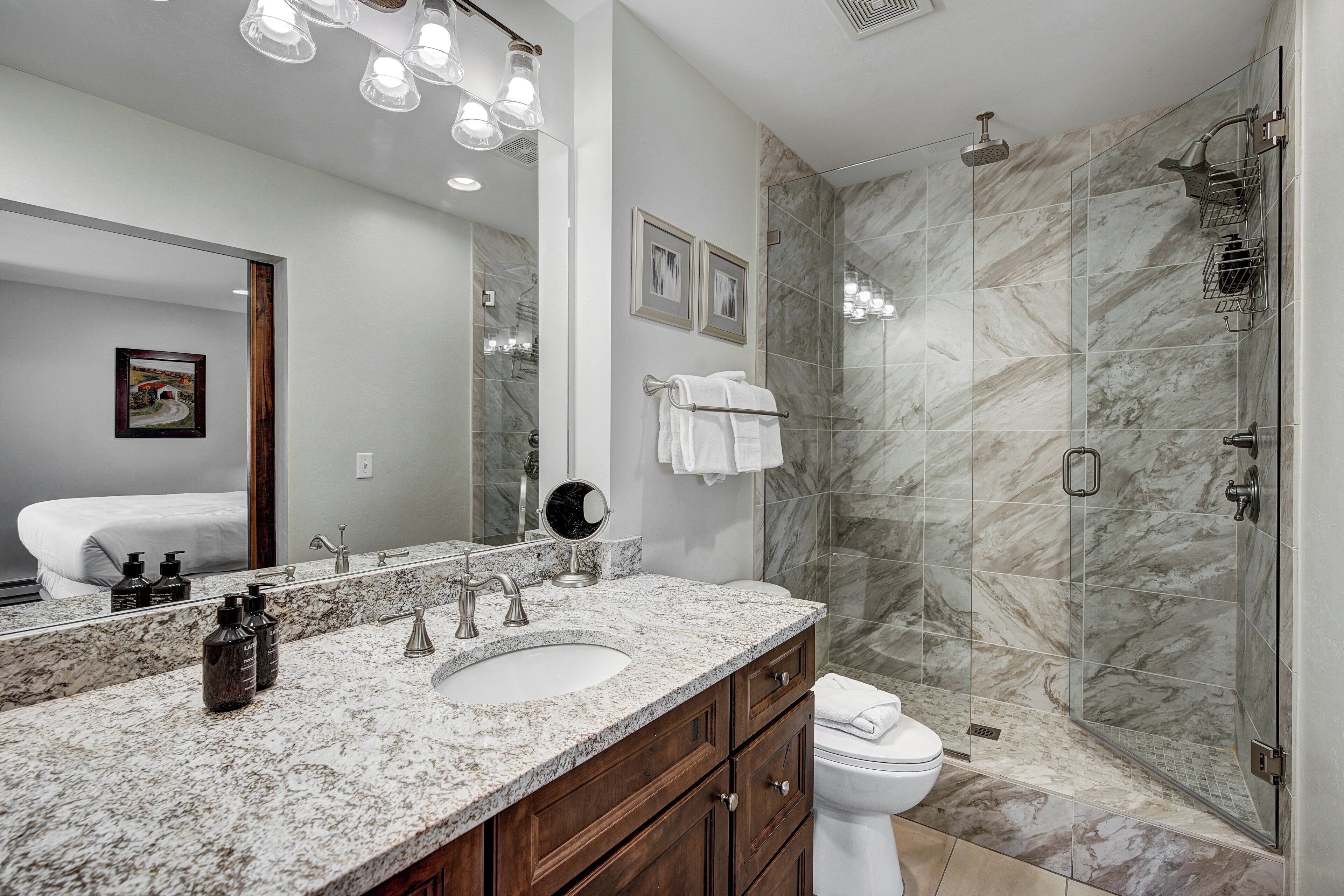 A modern bathroom with a marble sink, a large mirror, and a glass-enclosed shower.