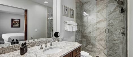 A modern bathroom with a marble sink, a large mirror, and a glass-enclosed shower.