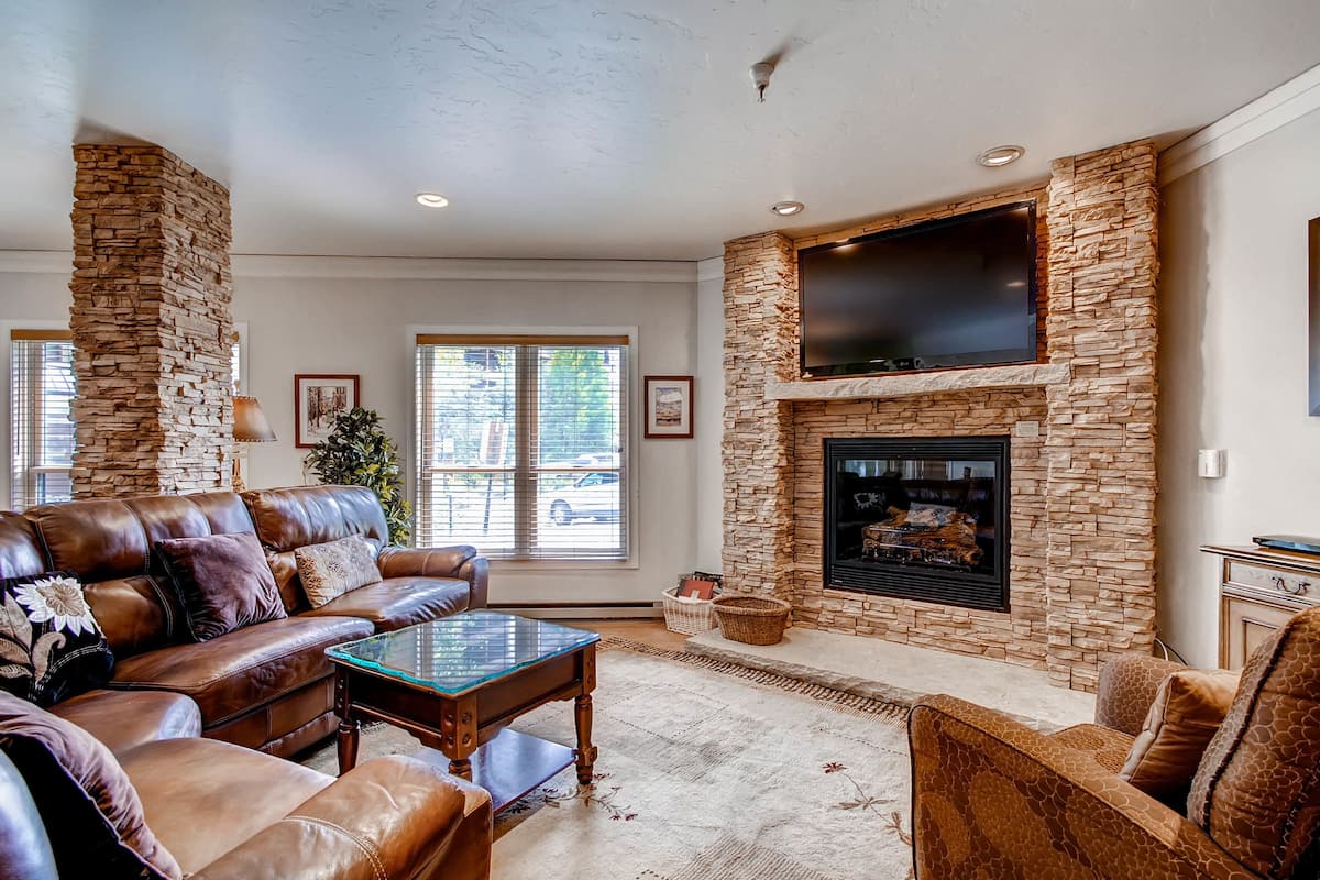 A living room with a stone fireplace, leather furniture, and a flat-screen TV mounted above it.