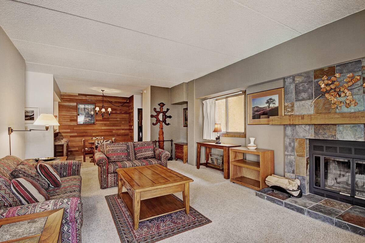 A spacious living room with a fireplace, wooden furniture, and a stone accent wall.