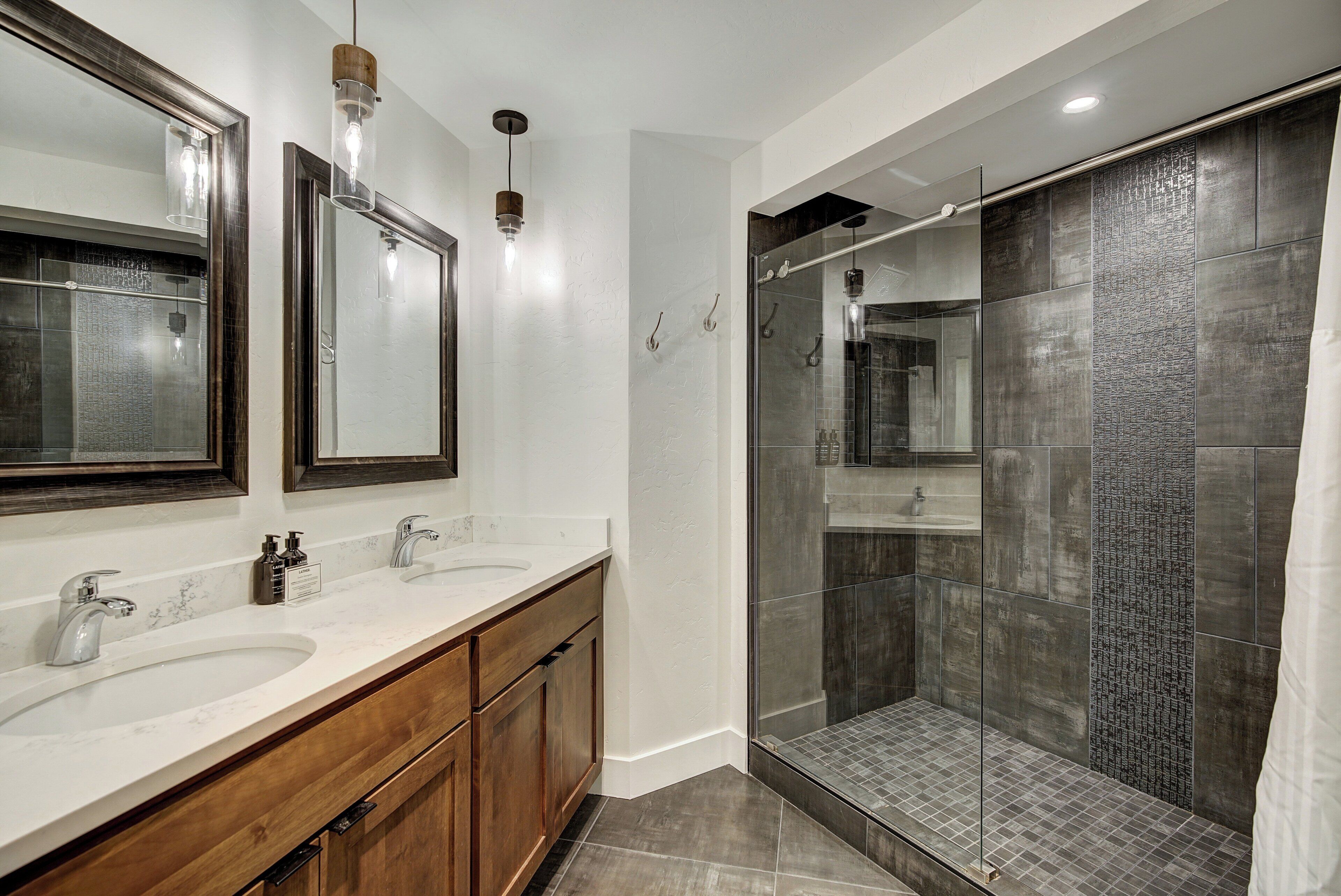 A modern bathroom with two sinks, wooden cabinets, and a glass-enclosed shower area.