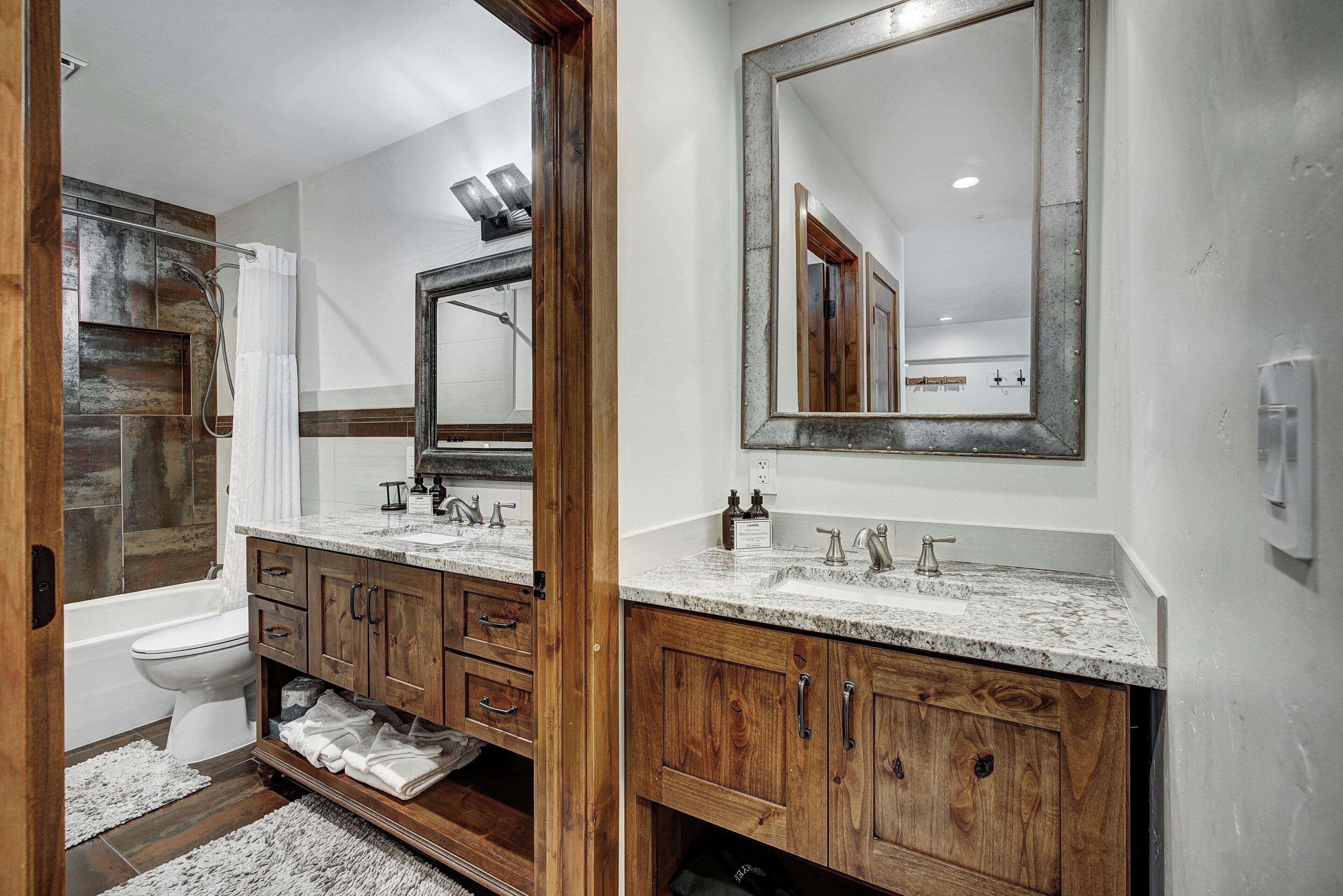A bathroom with a wooden vanity, a large mirror, a bathtub, and a toilet.