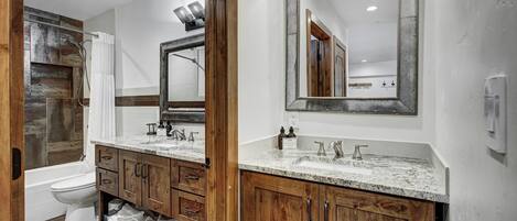 A bathroom with a wooden vanity, a large mirror, a bathtub, and a toilet.