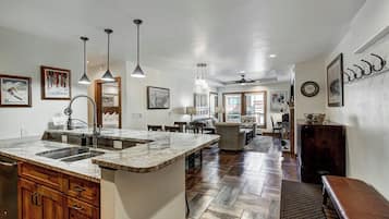 A spacious kitchen with a large island, wooden cabinets, and a stone countertop. There is a dining area with a table and chairs, and a living room with a sofa and a coffee table.