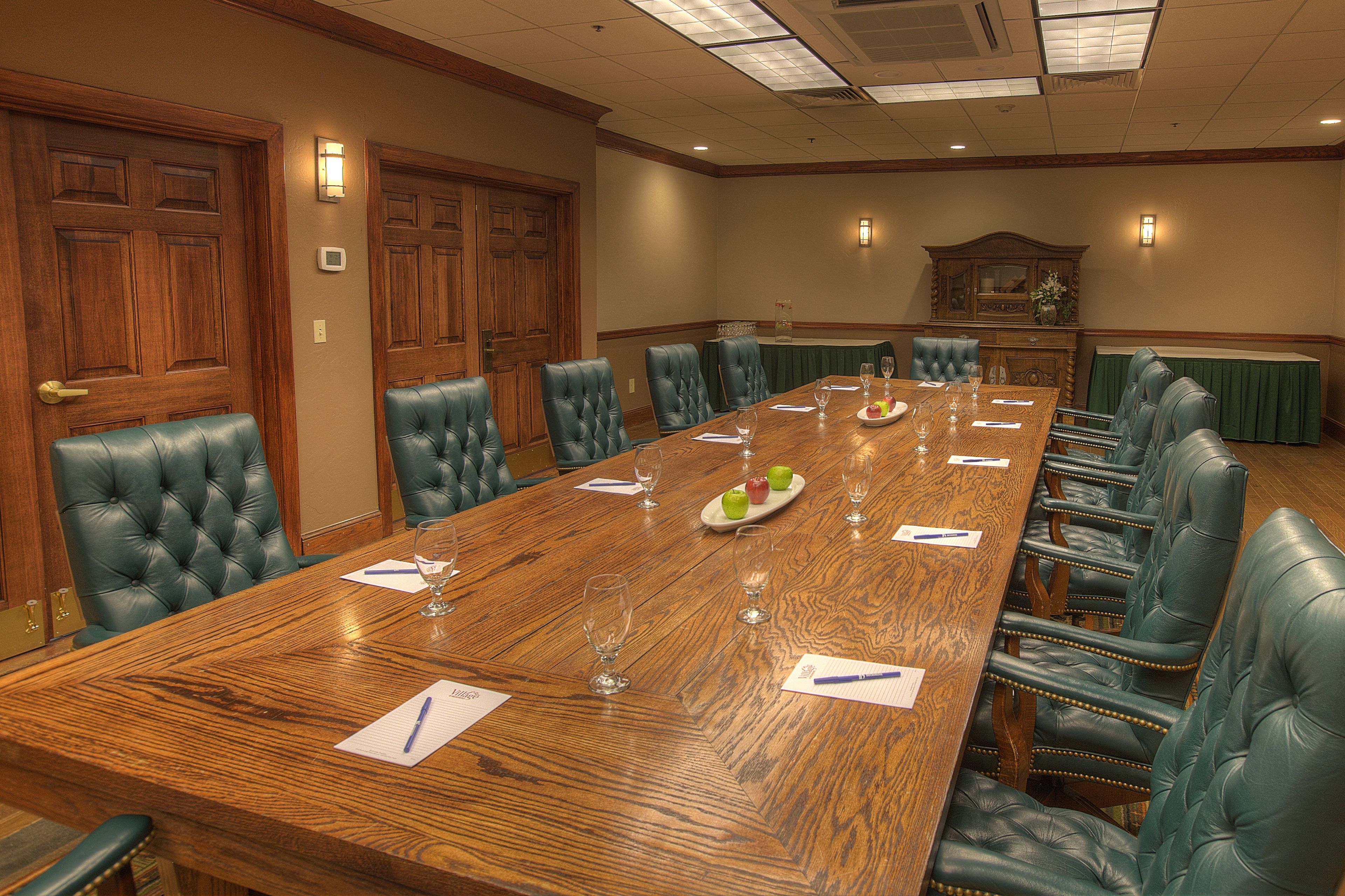 A conference room with a long wooden table, green leather chairs, and a chandelier.