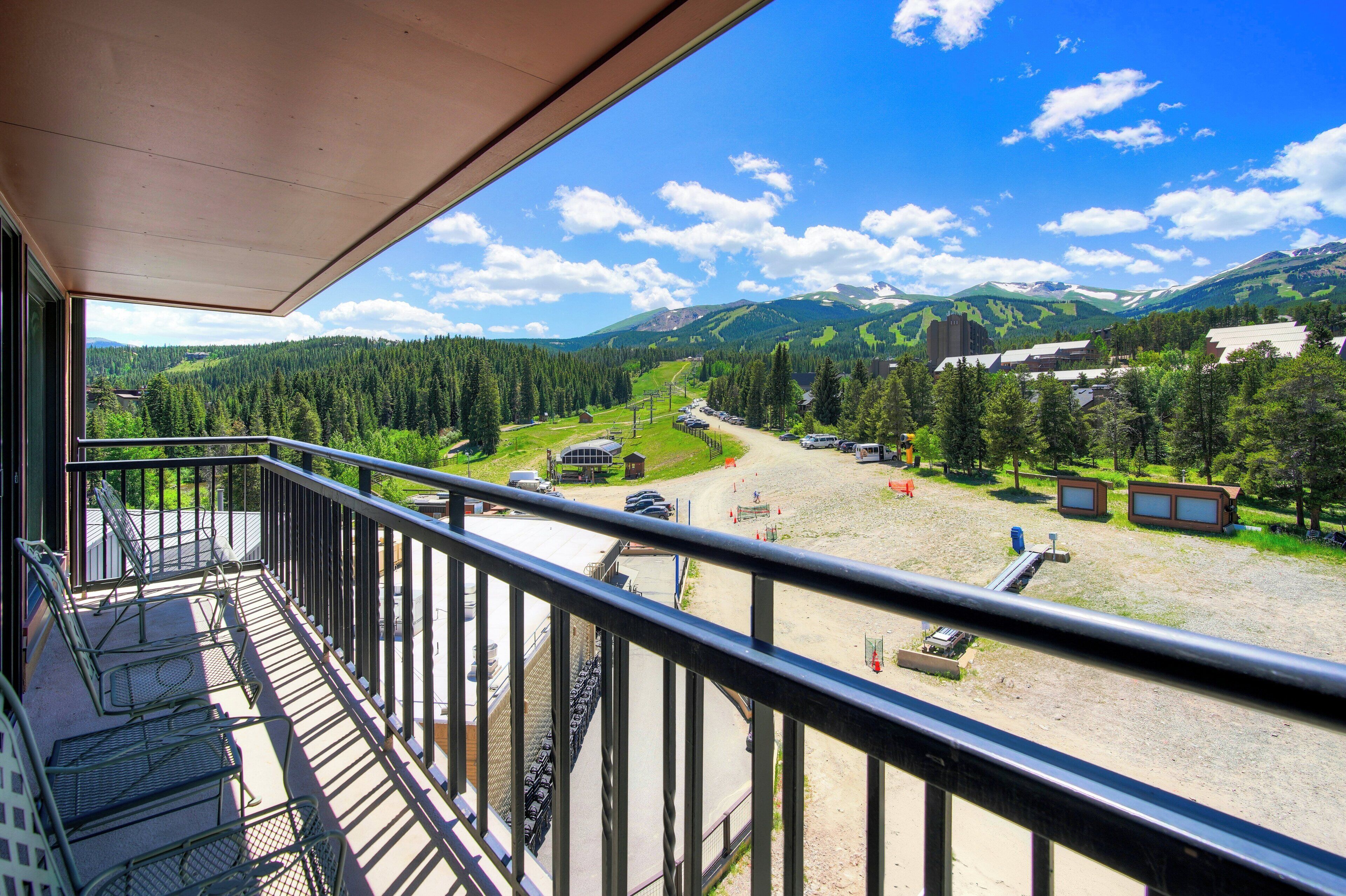 A balcony with a view of a mountainous landscape, a parking area, and a building with a sloped roof.