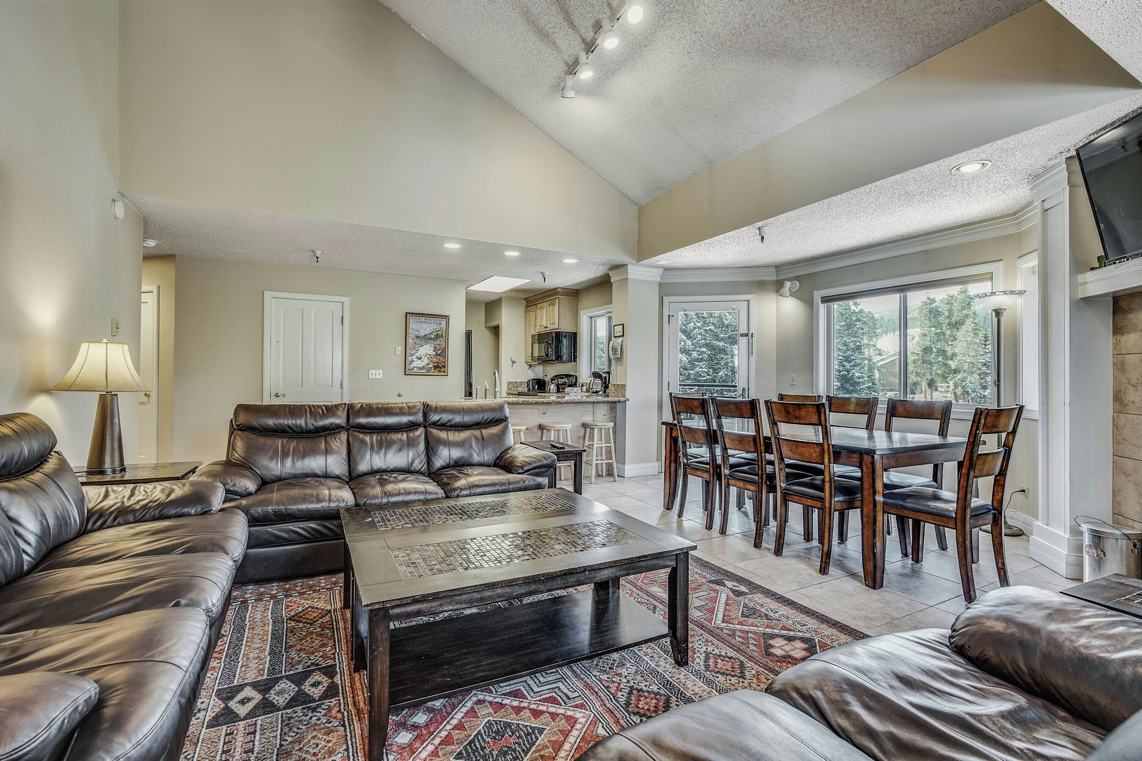 A spacious living room with a leather sectional sofa, a dining area with wooden chairs, and a kitchen in the background.