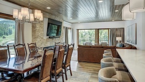 A spacious dining area with a large wooden table and chairs, a stone accent wall, and a television mounted above the table. - Village at Breckenridge, A Vail Resorts Property (Breckenridge)