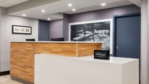 Un comptoir d’accueil avec un panneau décoratif en bois, un tableau encadré au mur et une grande affiche sur laquelle figure le mot « heureux ».