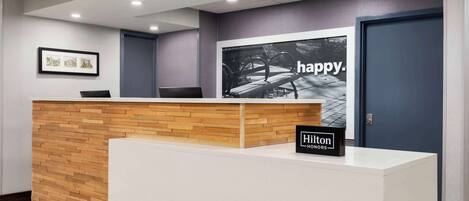 A reception desk with a wooden panel design, a framed picture on the wall, and a large poster with the word "happy."
