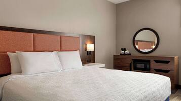 A hotel room with a large bed, a wooden headboard, a nightstand with a lamp, a dresser, a mirror, and a microwave.