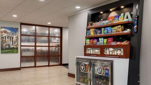 Un hall d’hôtel doté d’une grande fenêtre, un bar proposant divers produits emballés et une vitrine réfrigérée.