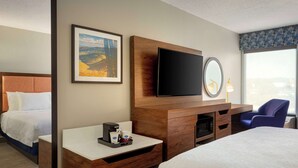 Une chambre d’hôtel équipée d’un lit, d’un bureau avec une machine à café, d’un téléviseur à écran plat, d’un miroir et d’une fenêtre donnant sur un paysage agréable.