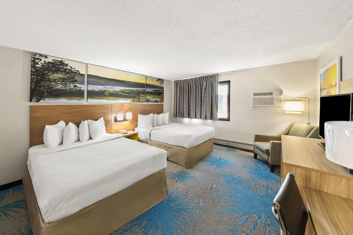 Ein Hotelzimmer mit zwei Betten, einem Schreibtisch, einem Sessel, einem Fernseher und einem großen Gemälde an der Wand.