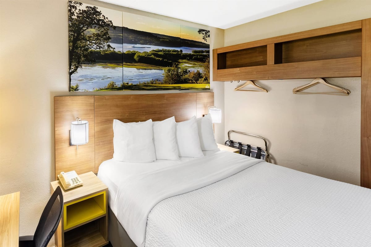 Ein Hotelzimmer mit einem Bett, einem Nachttisch mit Lampe, einem Telefon und einem Landschaftsbild.