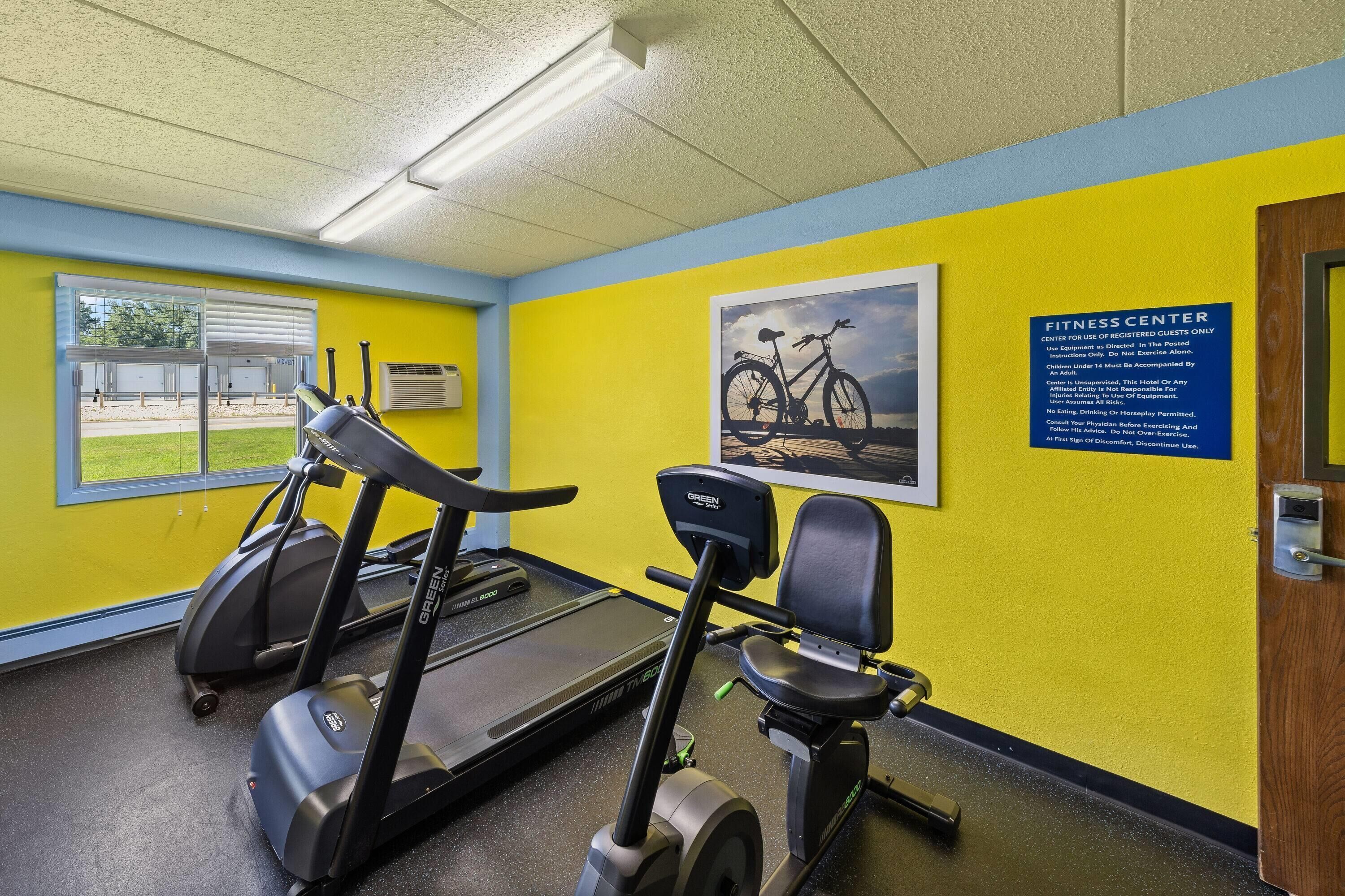 A fitness center with treadmills and a stationary bike, a window with a view of the outdoors, and a sign indicating the center is for registered guests only.