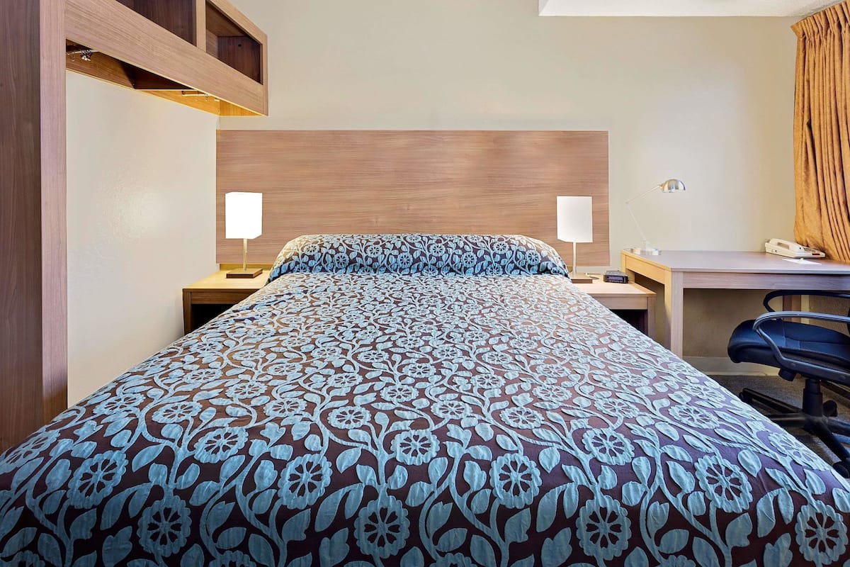 Ein Hotelzimmer mit einem Bett, zwei Nachttischlampen, einem Schreibtisch mit Stuhl und einem Telefon.