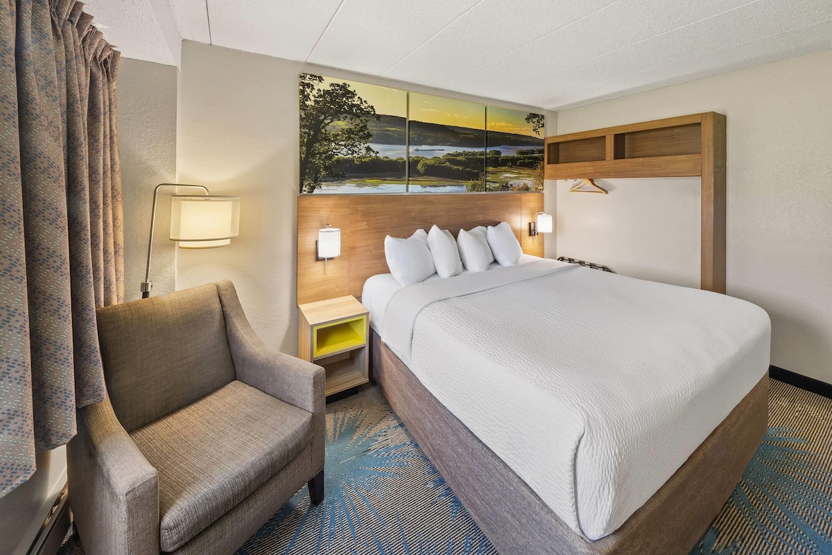 Ein Hotelzimmer mit einem großen Bett, einem Sessel, einem Nachttisch und einer Wandlampe.