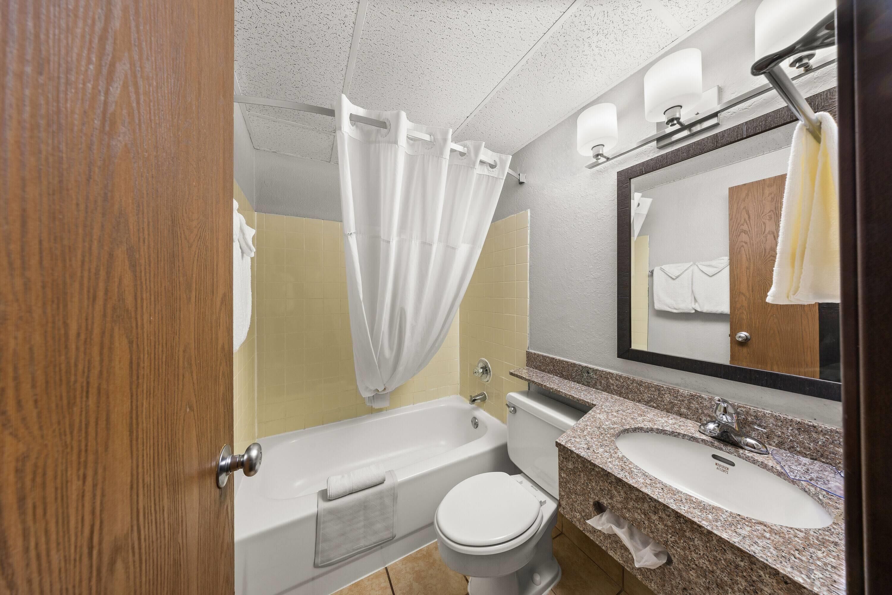 Un baño con bañera, inodoro, lavamanos y espejo.