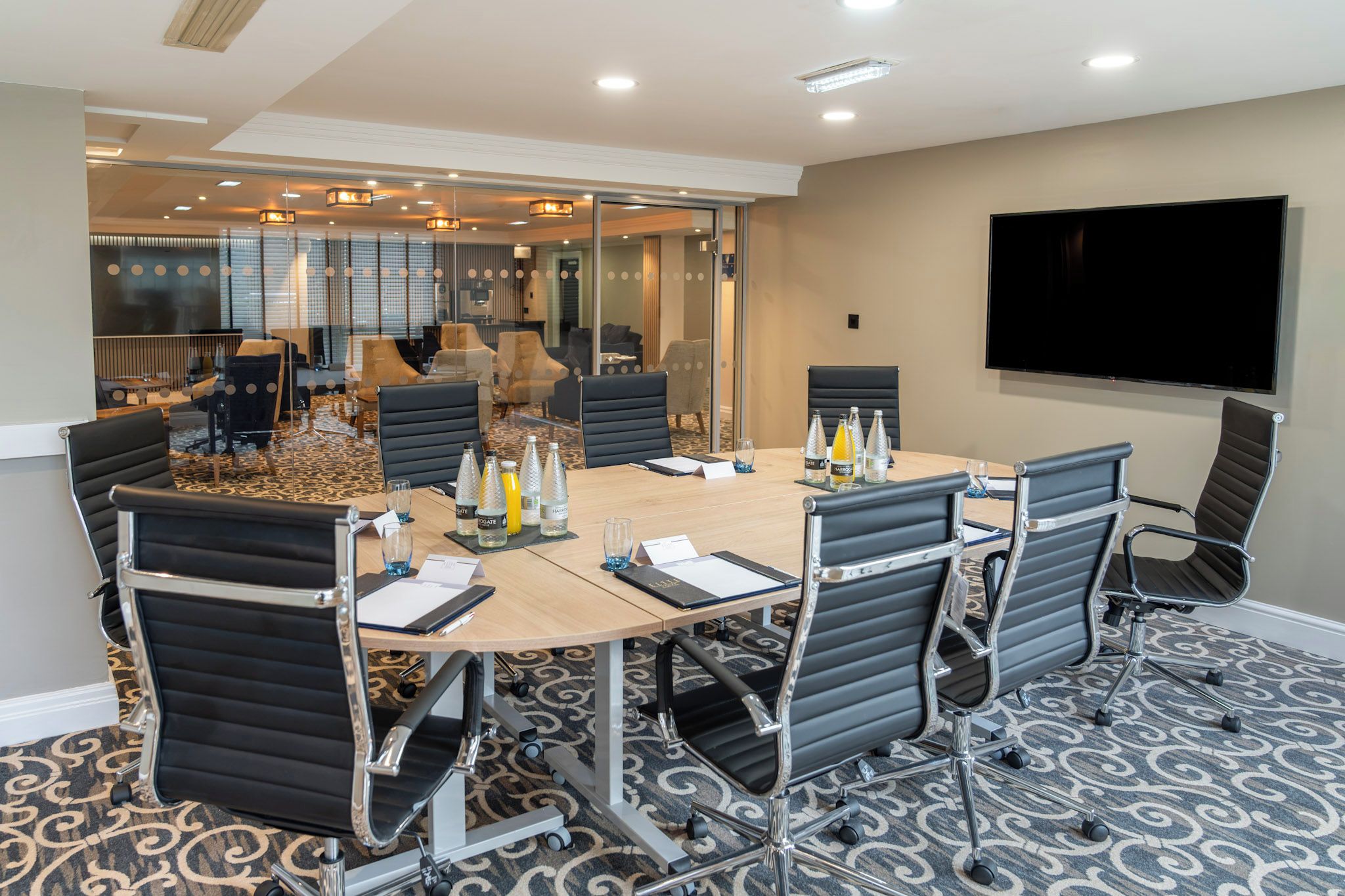 A conference room with a large table, multiple chairs, and a flat-screen TV on the wall.
