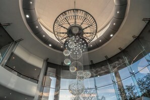 A modern atrium with a large circular skylight, a central chandelier, and glass railings.