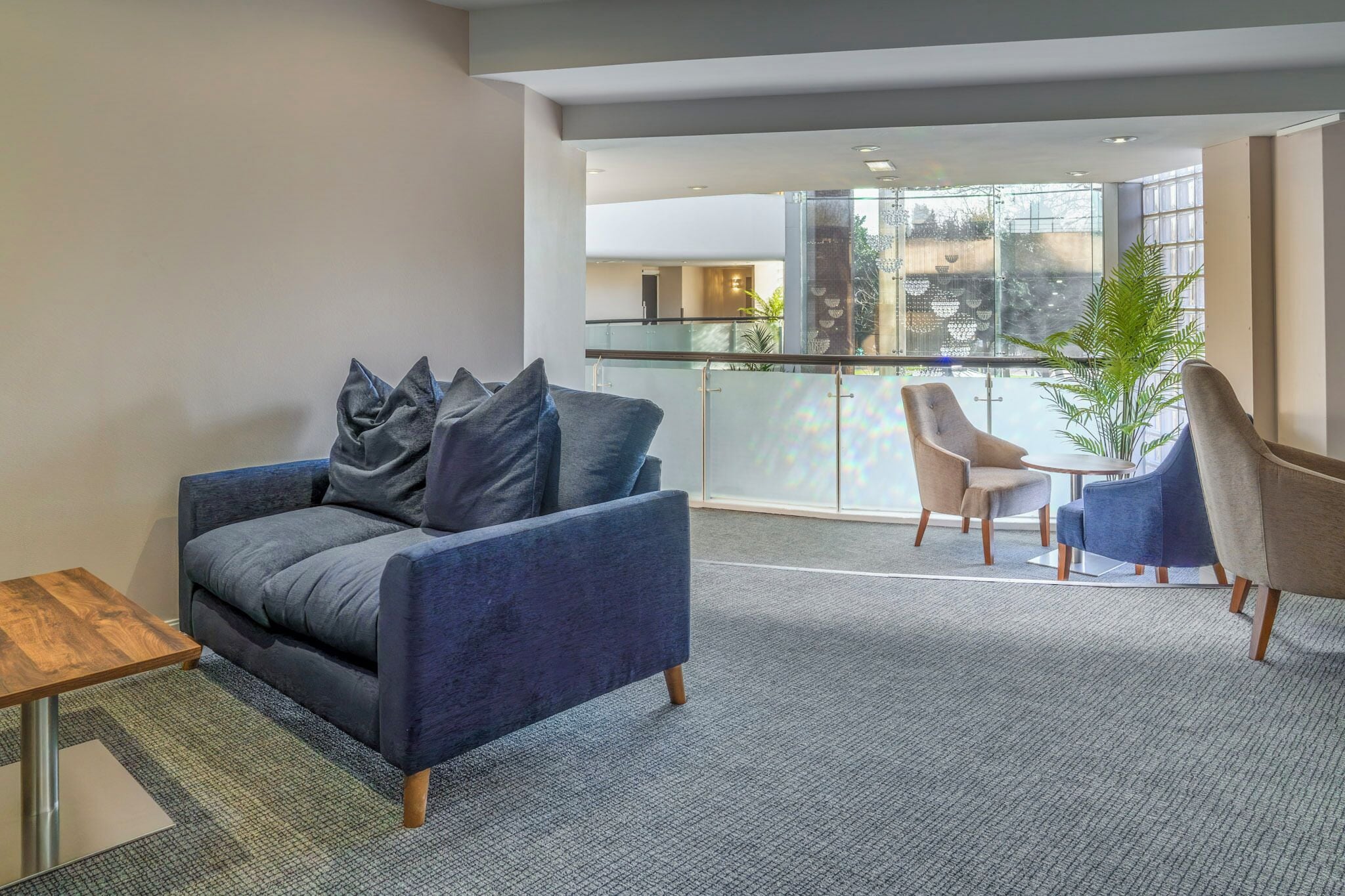 A modern living room with a grey sofa, a small wooden table, and a balcony with a glass railing.